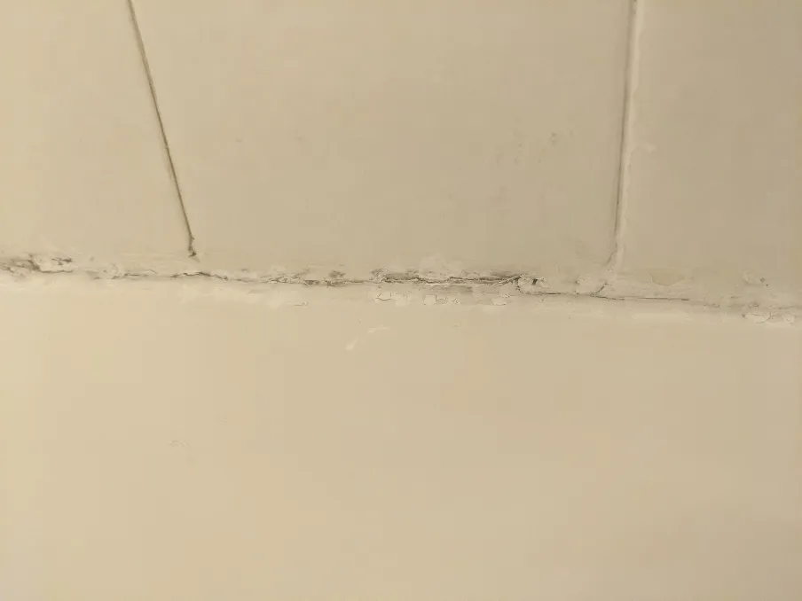 Poorly sealed edge between a broken fiberglass tub and some contractor grade tiles
