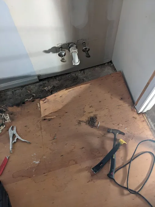 The underlayment of a floor is coming up slowly. Hand tools lay next to a pile of staples.