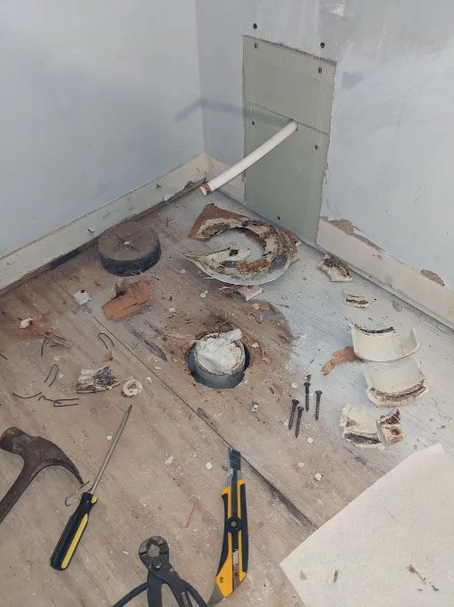 A toilet flange lays in pieces on the floor, surrounded by tools