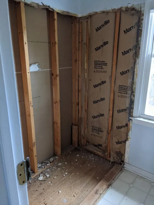 A picture of the place where a tub used to be. The walls have been cut away, leaving only structural studs