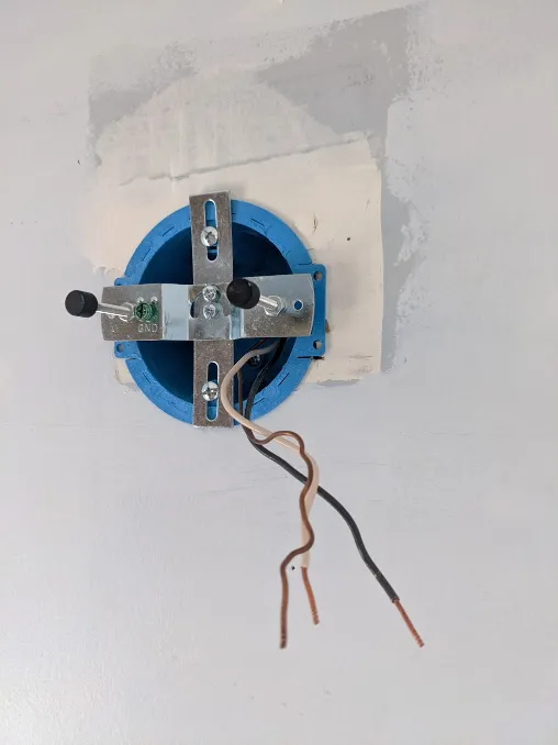 An old-work electrical box has been installed on a wall. Wires hang out of it