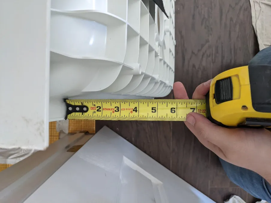 A measuring tape shows the amount of space left under a shower pan. Much less than 5 inches