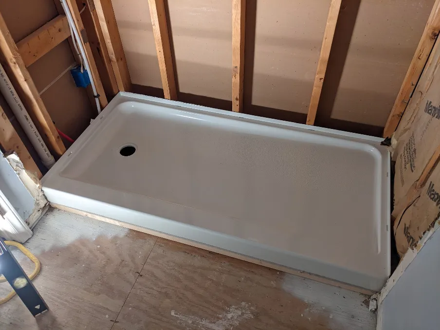 A shower pan sits atop the cement board, showing that it does, in fact, fit