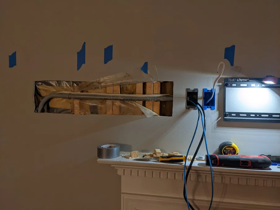 A gray plastic pipe is visible inside the wall through the hole. Wires hang out of the electrical boxes
